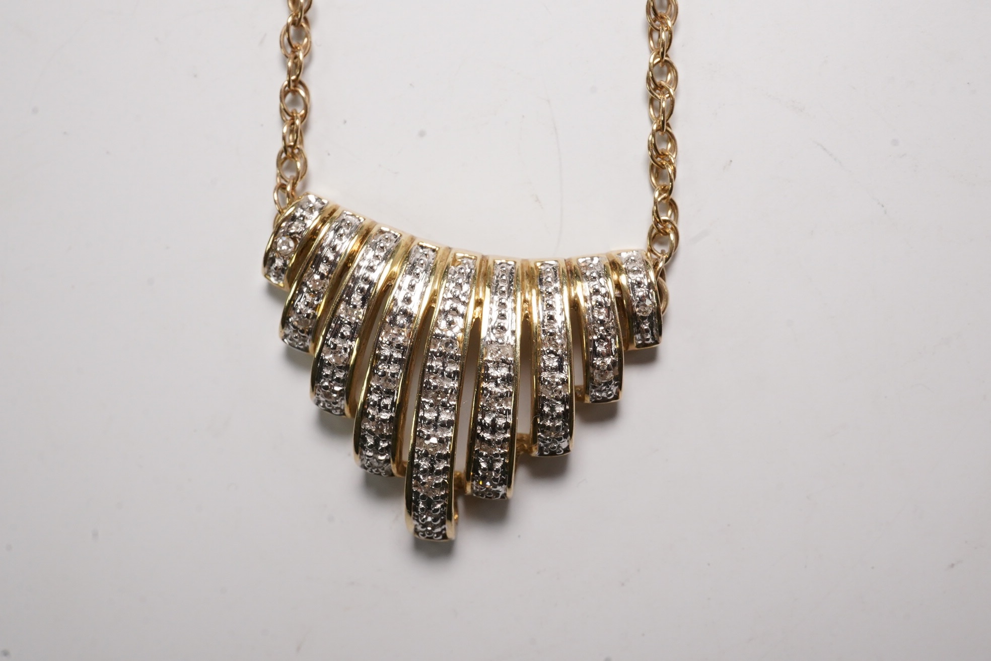 A yellow metal and diamond chip set fan shaped pendant, width 22mm, on a 375 chain, 40cm, gross 5.6 grams.
